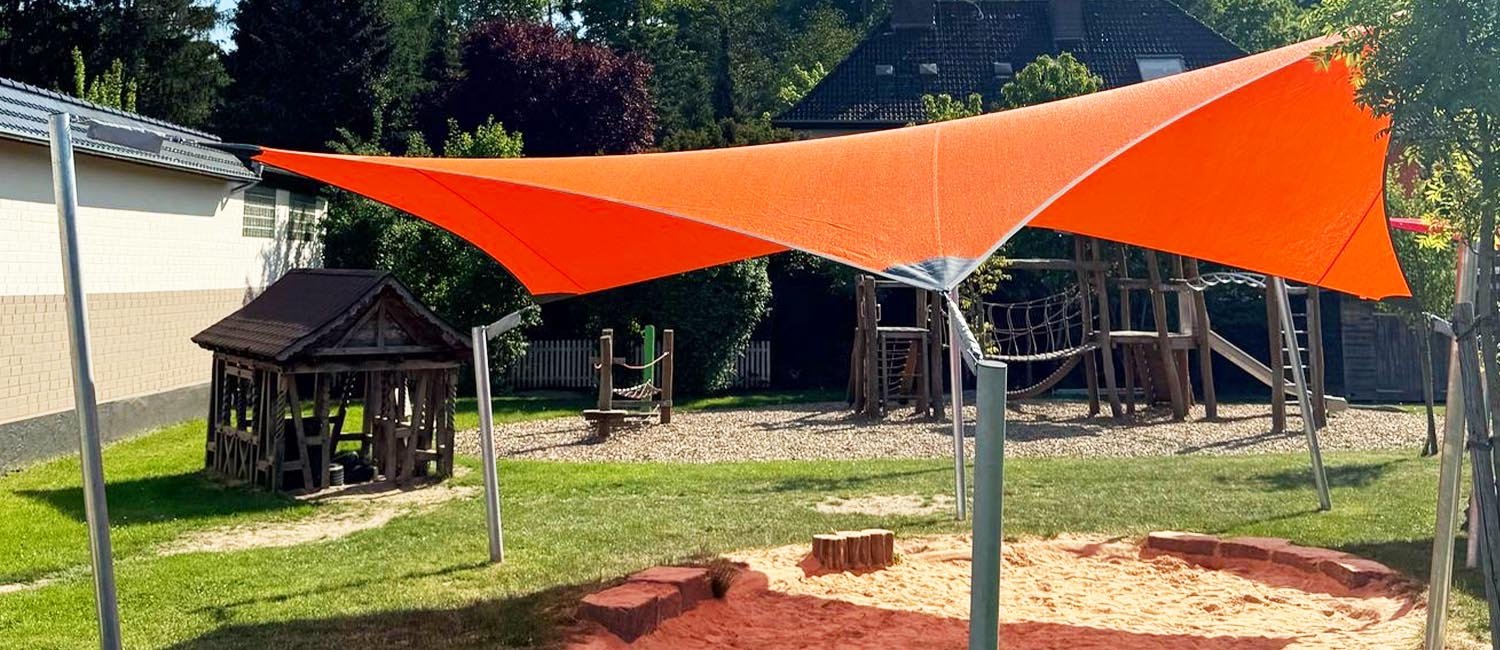 Vela ombreggiante fissa arancione sopra l'area giochi di un asilo